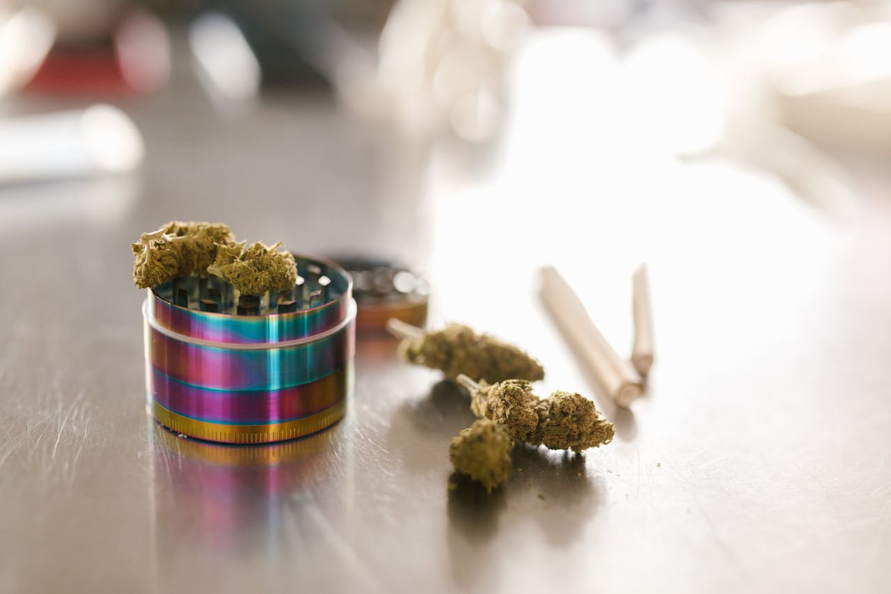 about-07 Cannabis buds with a colorful grinder on a reflective surface in natural light.